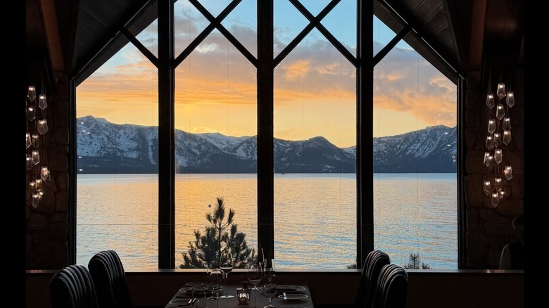 The sun sets behind snow-covered mountains through floor-to-ceiling windows at The Edge in Lake Tahoe.