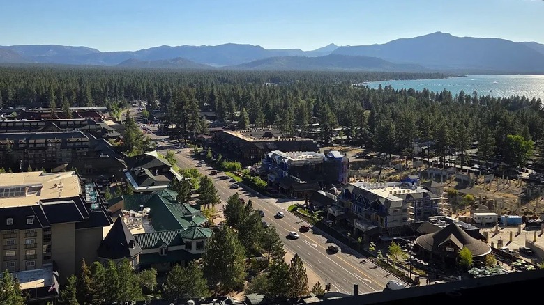 Pines and the buildings of Interstate, Nevada, surround Lake Tahoe, with tall mountains in the background.