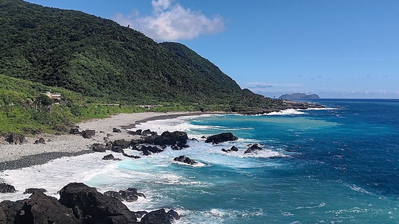 A blue coastline, a gray shore, and green hillls against a bright blue sky at Orchid Island in Taiwan