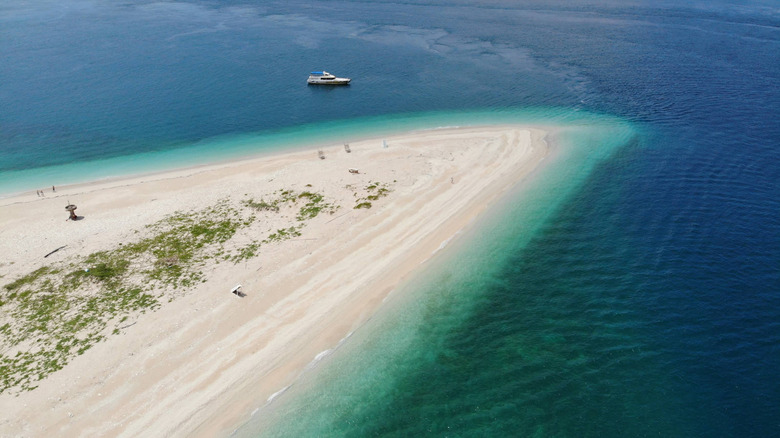 White sands are ringed by teal water and dark blue ocean at Taiwan's Pengpeng Beach sandbar as a boat drives by