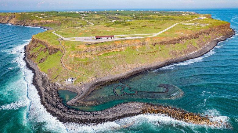 The green island of Qimei from above, nestled in a rough blue sea, with the ancient Double-Heart of Stacked Stones seen near the shore