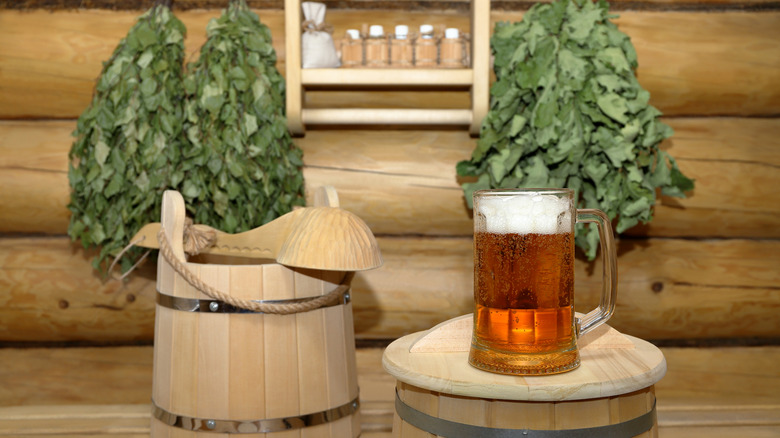A mug of beer next to traditional spa supplies like sauna whisks and a bucket with a ladle