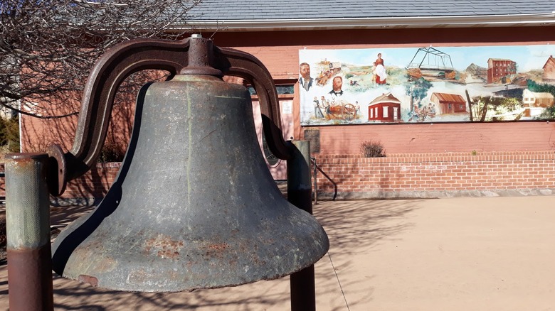 Large antique bell outside brick building with a mural at the Taylor Arizona Museum.