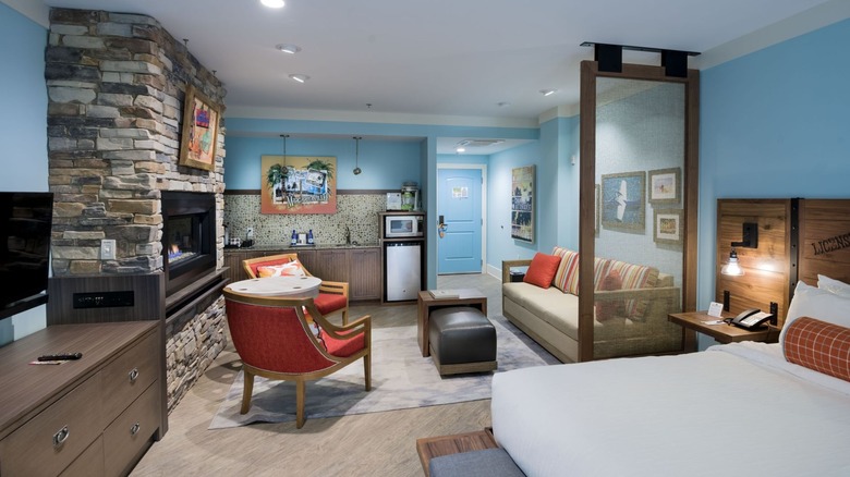 An interior view of a Compass Hotel suite, with sofa, drawers, a wide-screen television, and throw-pillows on the beds labeled "Wanderer"