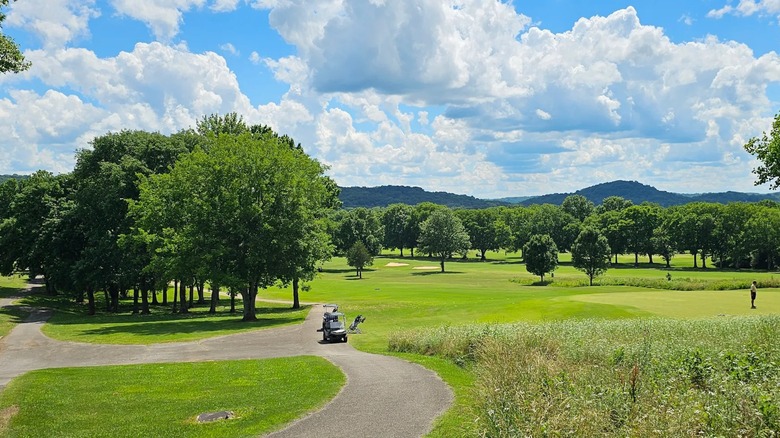 A view of a golf cart on the fairway with rolling terrain and trees in the background of Harpeth Hills, Nashville
