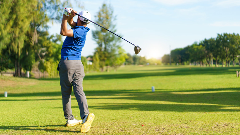 A single male golfer holding a driver in post-tee off stance on a golf course
