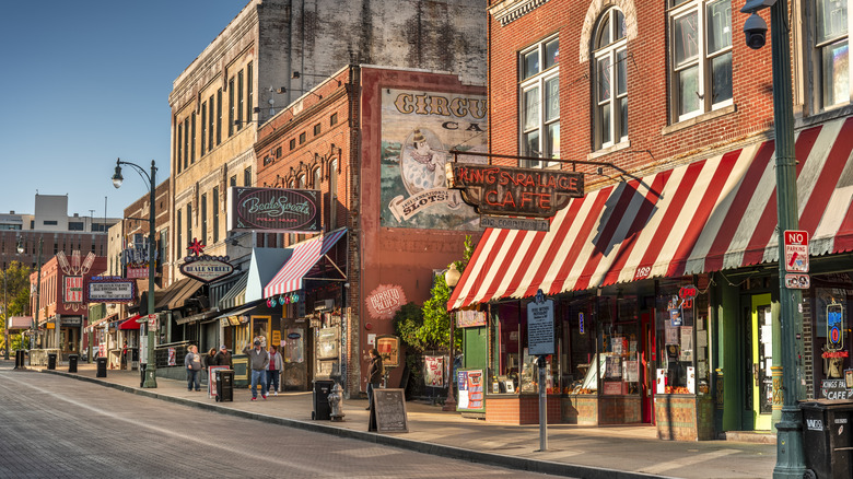 Neon signs, shopfronts, cafes, music venues, and people along Beale Street in Memphis on a sunny day.