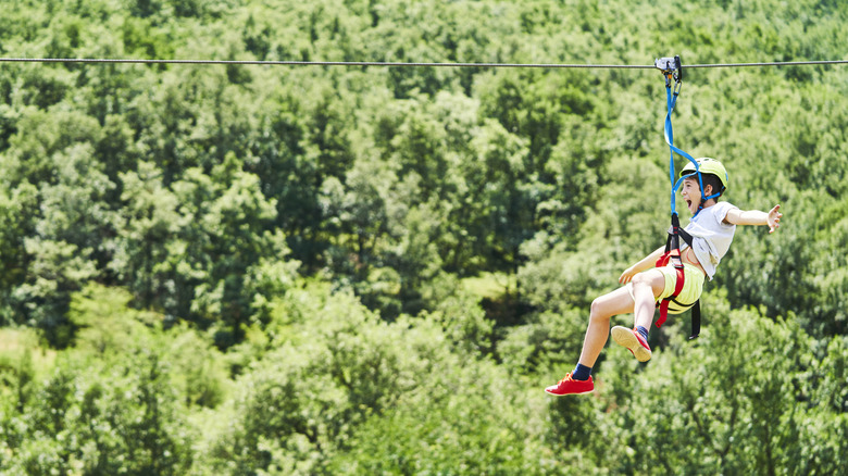 Young boy ziplining above forest