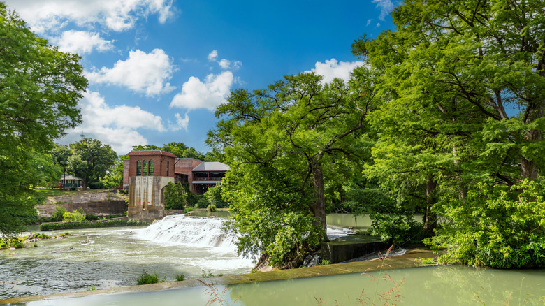 River with a small waterfall flowing past an old brick building in Seguin, Texas