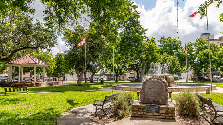 Lush park with a stone monument in the foreground, benches, and a gazebo in Seguin, Texas