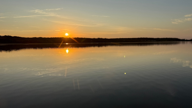 The sun setting over Cedar Lake in Cleburne State Park, Texas; the water and trees are lit up by the orange sunset