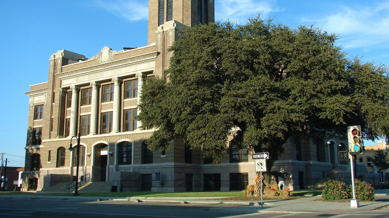 The couthouse in Cleburne, Texas, under a blue sky with a tree in front