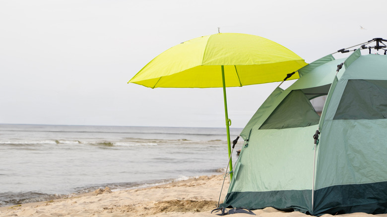 Green tent with a yellow umbrella on sandy beach