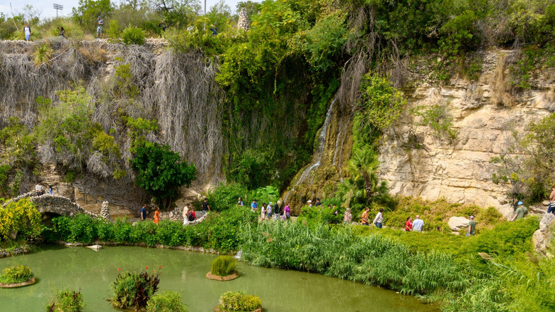 People walking along a walkway next to a pond, leading to the waterfall in the Japanese Tea Garden