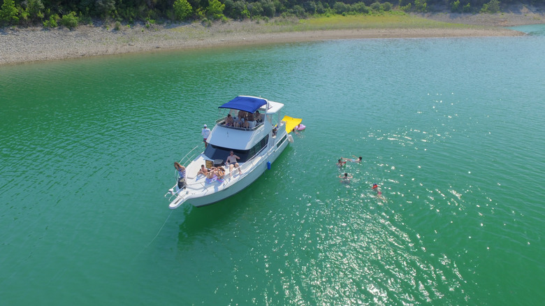 A party boat with people swimming and sunbathing anchored in a quiet area of Lake Travis.