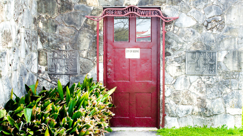 Vintage red door in the city of Boerne, Texas on a stone wall with plants in front.