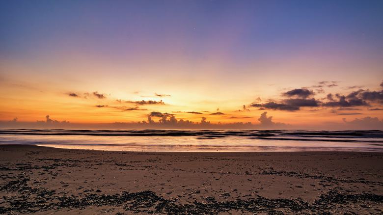 Sunset at the beach, brown sand and calm waves