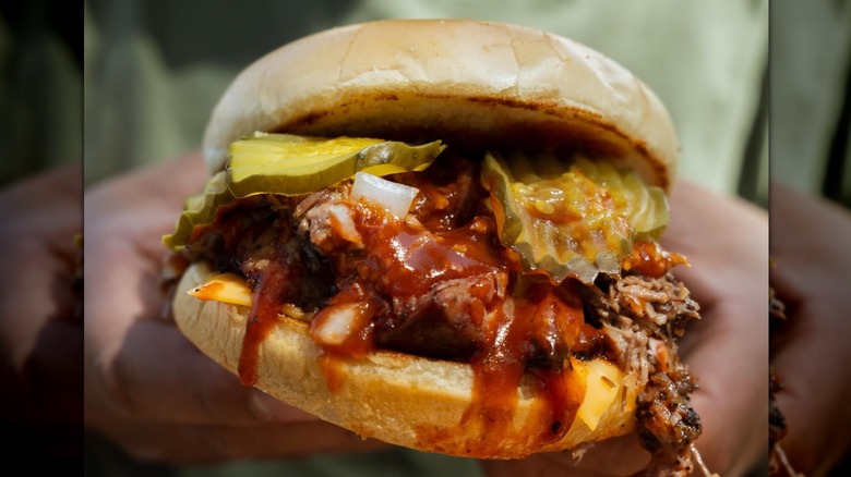 A closeup of a burger from Stanley's Famous Pit Barbecue with brisket, pickles, BBQ sauce.