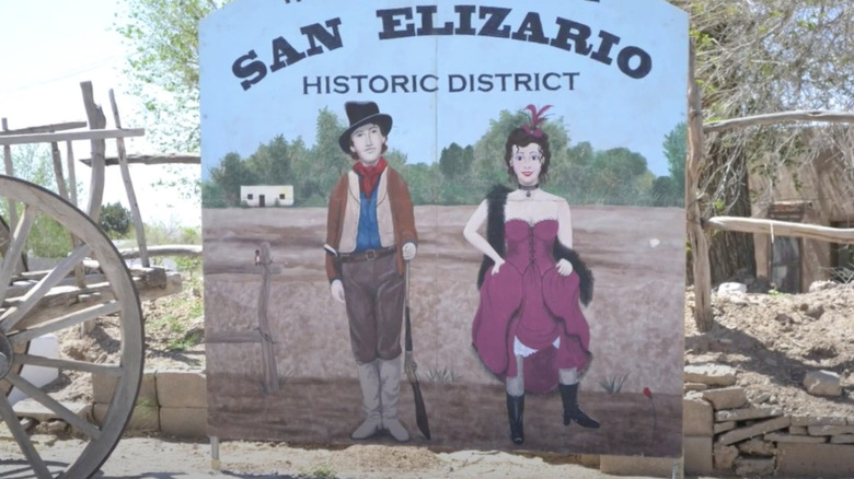 sign with people and text in front of wooden fence and green trees