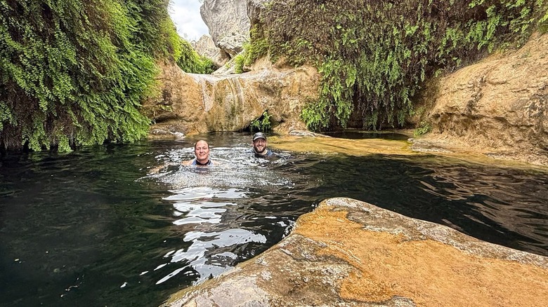 Two people swimming in the deep pools at the Blanco River Narrows surrounded by cliffs covered in maidenhair ferns.