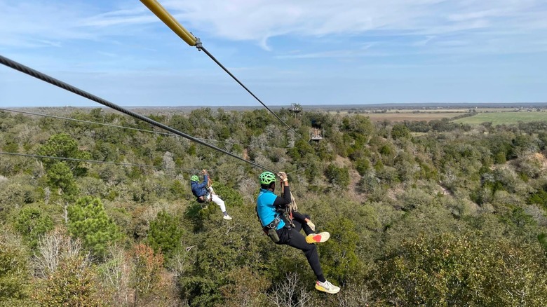 Two people zip lining over the trees at Zip Lost Pines located in McKinney Roughs Nature Park in Texas