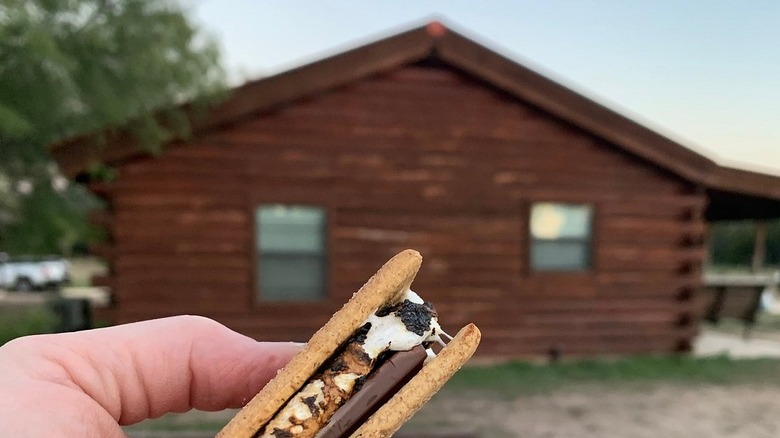 Hand holding s'mores in front of cabin at Nueces River RV and Cabin Resort