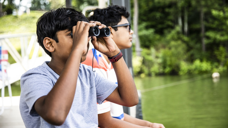 Kid looking into binoculars by a body of water