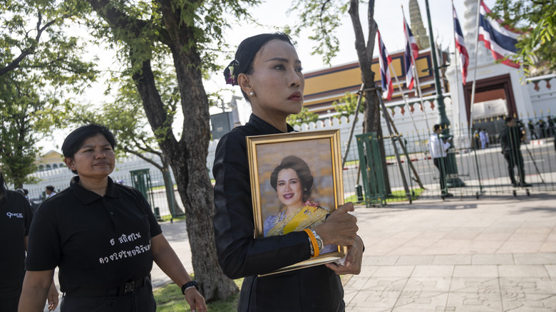 Thai mourner at the Grand Palace in Bangkok holds a framed photo of Queen Sirikit