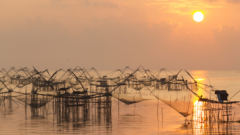 Traditional fishing nets suspended over the water at sunset at Songkhla Lake, Thailand.