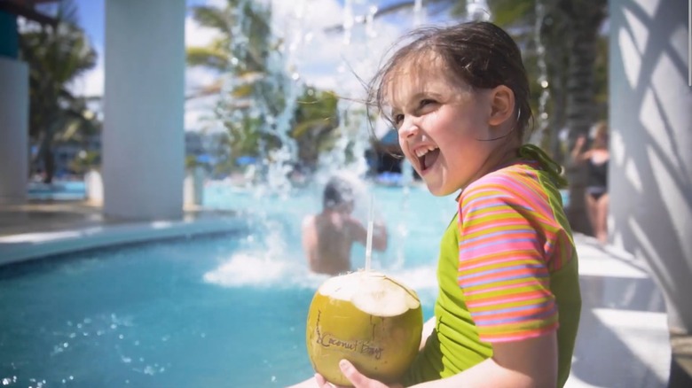 A laughing girl holds a coconut drink by the pool