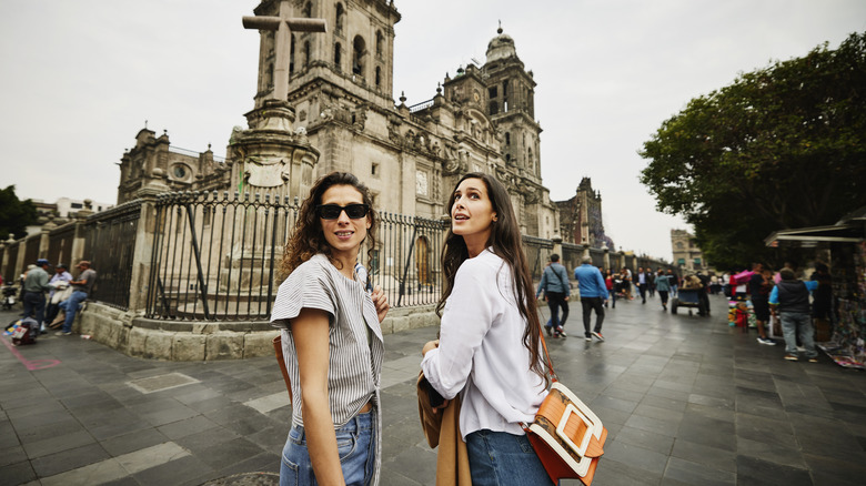 Two friends with dark hair look around the main plaza in Mexico City