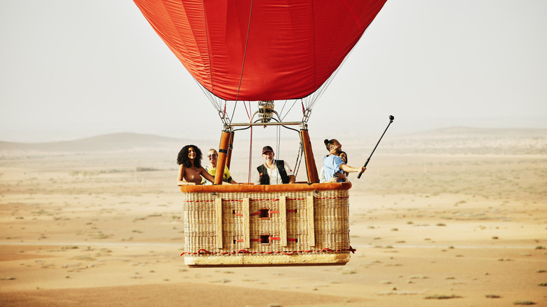 Five people ride a red hot air balloon in the Moroccan desert