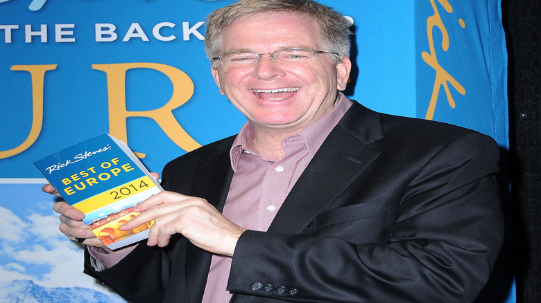 Travel writer Rick Steves poses with one of his books in front of a book poster