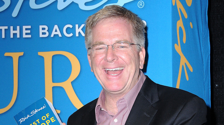 Travel writer Rick Steves poses with one of his books in front of a book poster