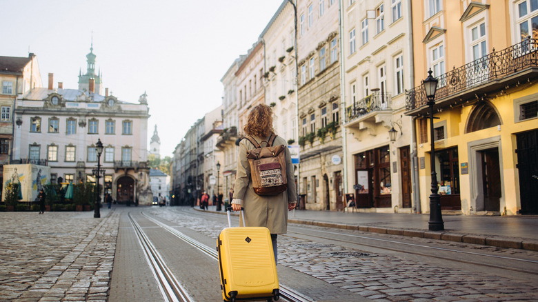Woman walks down European street with yellow suitcase