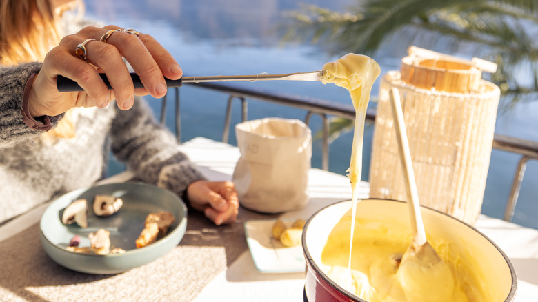 woman in knit sweater dipping bread into cheese