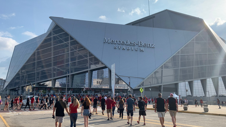 Exterior view of glass and steel Mercedes-Benz Stadium in Atlanta, Georgia with throngs of fans wearing black and red entering for a football game