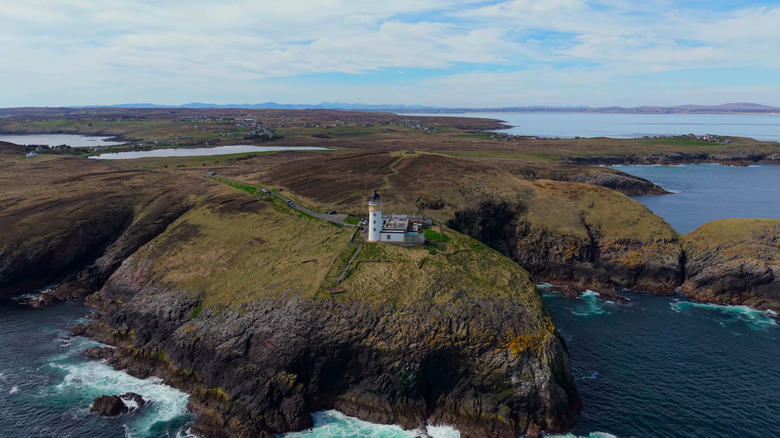 A wide angle, aerial view of Dunnet Head Lighthouse at the edge of a cliff