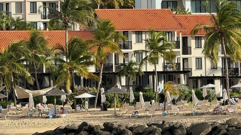 Exterior view of the hotel and beach at Sandals Grenada with people, lounge chairs, and umbrellas in the foreground