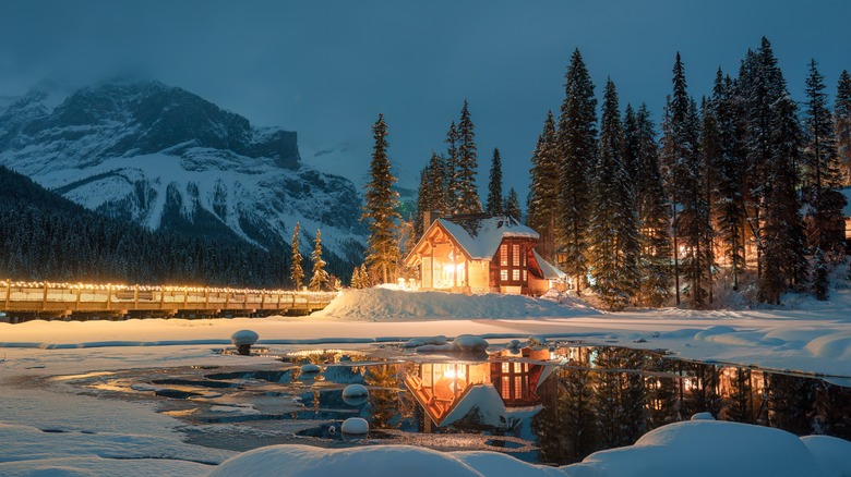 A cozy looking wooden home with big windows, coverd in snow, with a mountain the in background