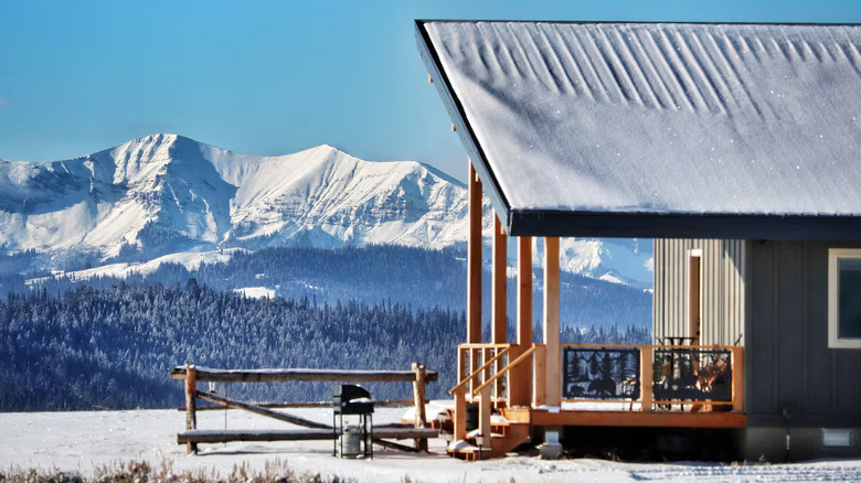 The front porch of a cabin in a snowy landscape with mountains in the background.