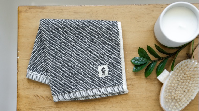 Folded gray towel sits next to candle and brush on wooden table top