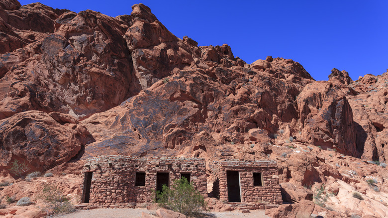 Stone shelters in front of a red rock wall under a blue sky in Valley of Fire State Park