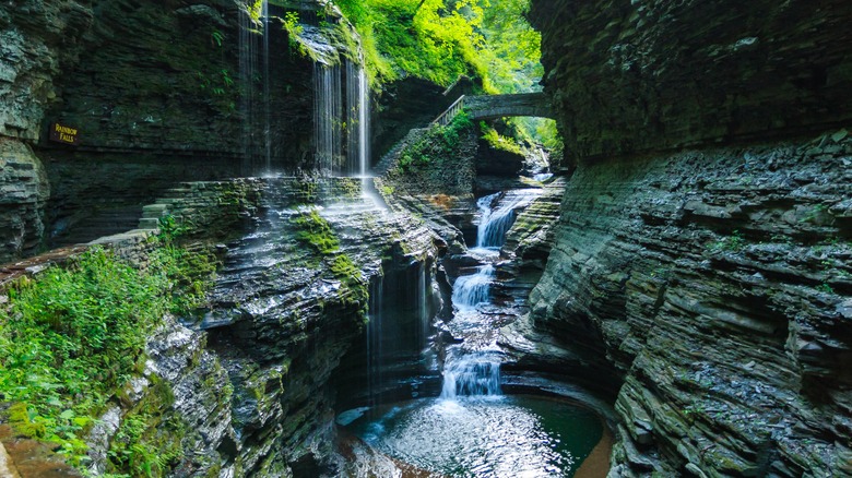 Rainbow Falls, with a bridge between two rock cavern walls and multiple waterfalls flowing into a pool