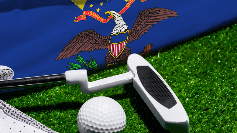 Golf ball and club with flag of North Dakota on green grass