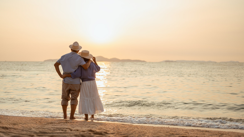 Elderly couple standing along a beach at sunset