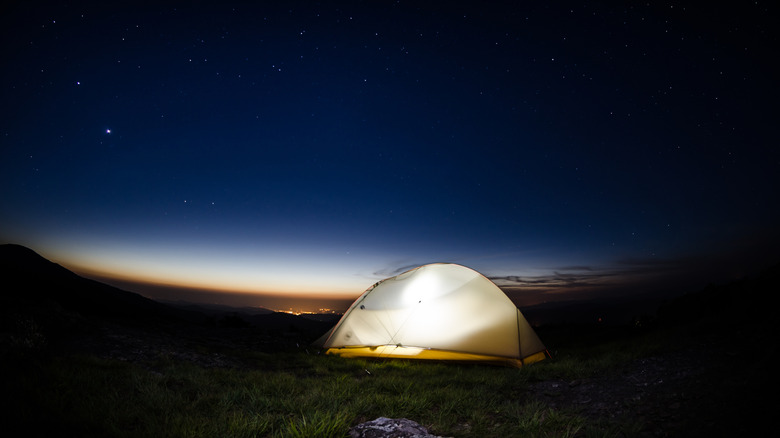 A glowing tent lit in the evening under a starry sky