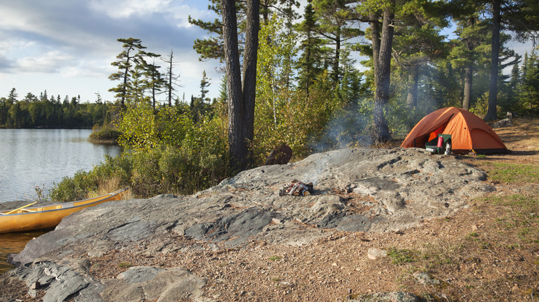 An orange tent by a rocky bluff near a lake
