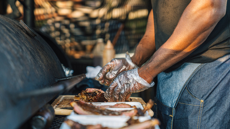 Someone plating barbecued meat next to a smoker