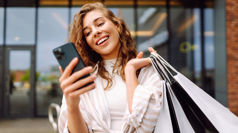 Woman holding shopping bags while checking her phone